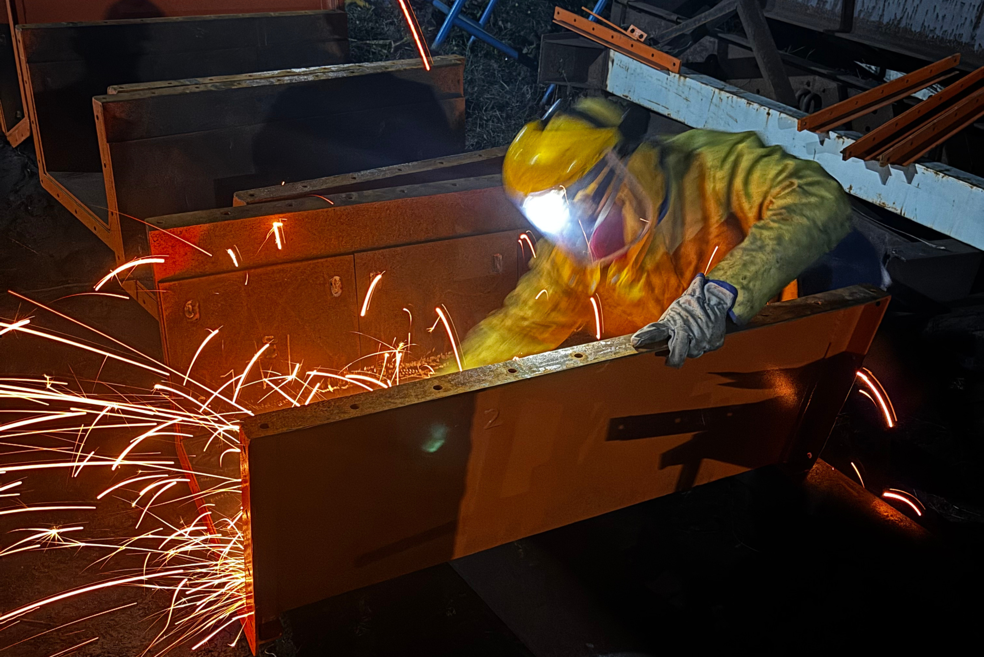 Une personne portant un équipement de protection complet, y compris un masque de soudage et des gants, effectue des travaux sur une structure métallique