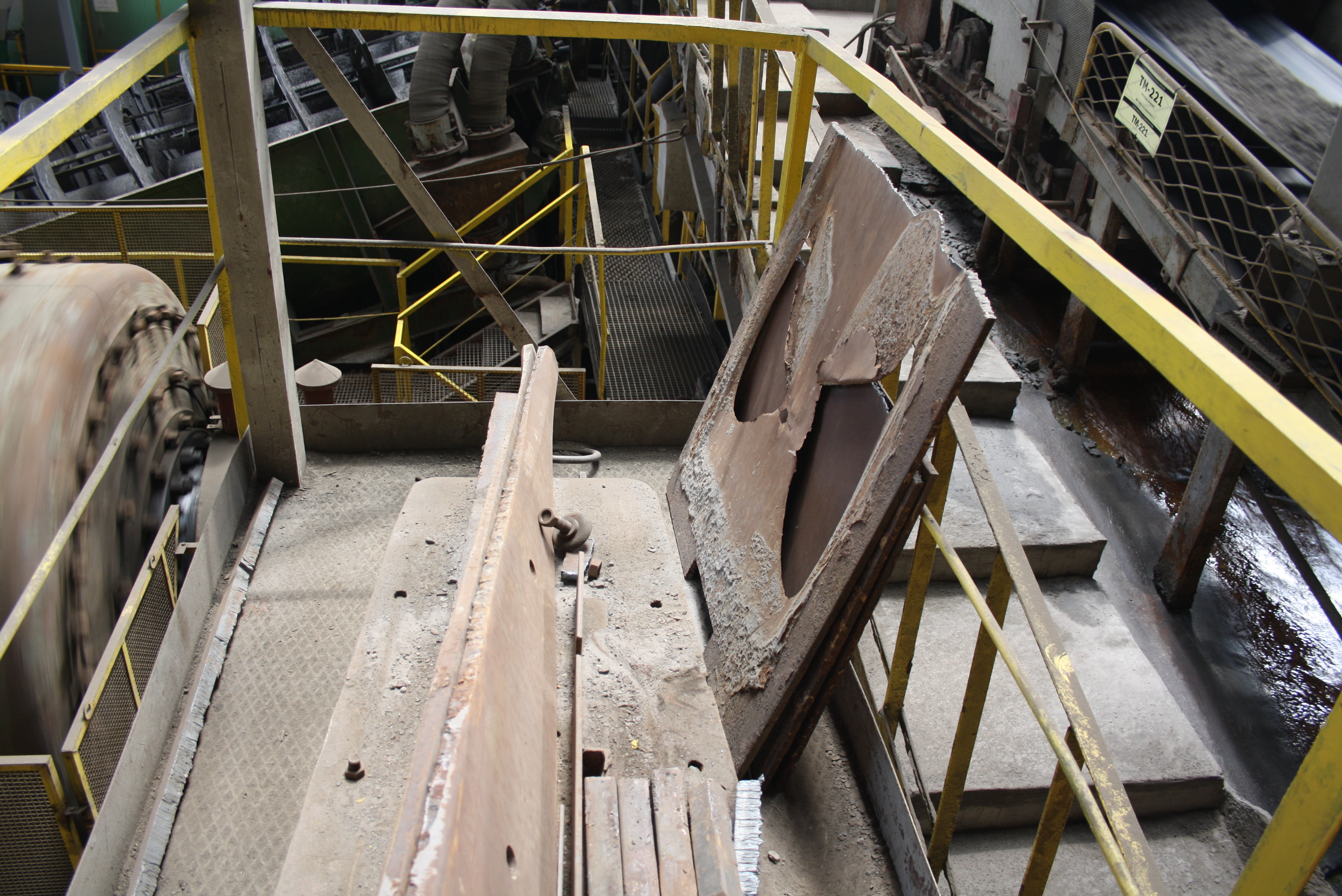 Une vue en plongée d'une passerelle industrielle avec des garde-corps jaunes, montrant des plaques métalliques usées et des composants lourds dans une usine ou une installation de production.