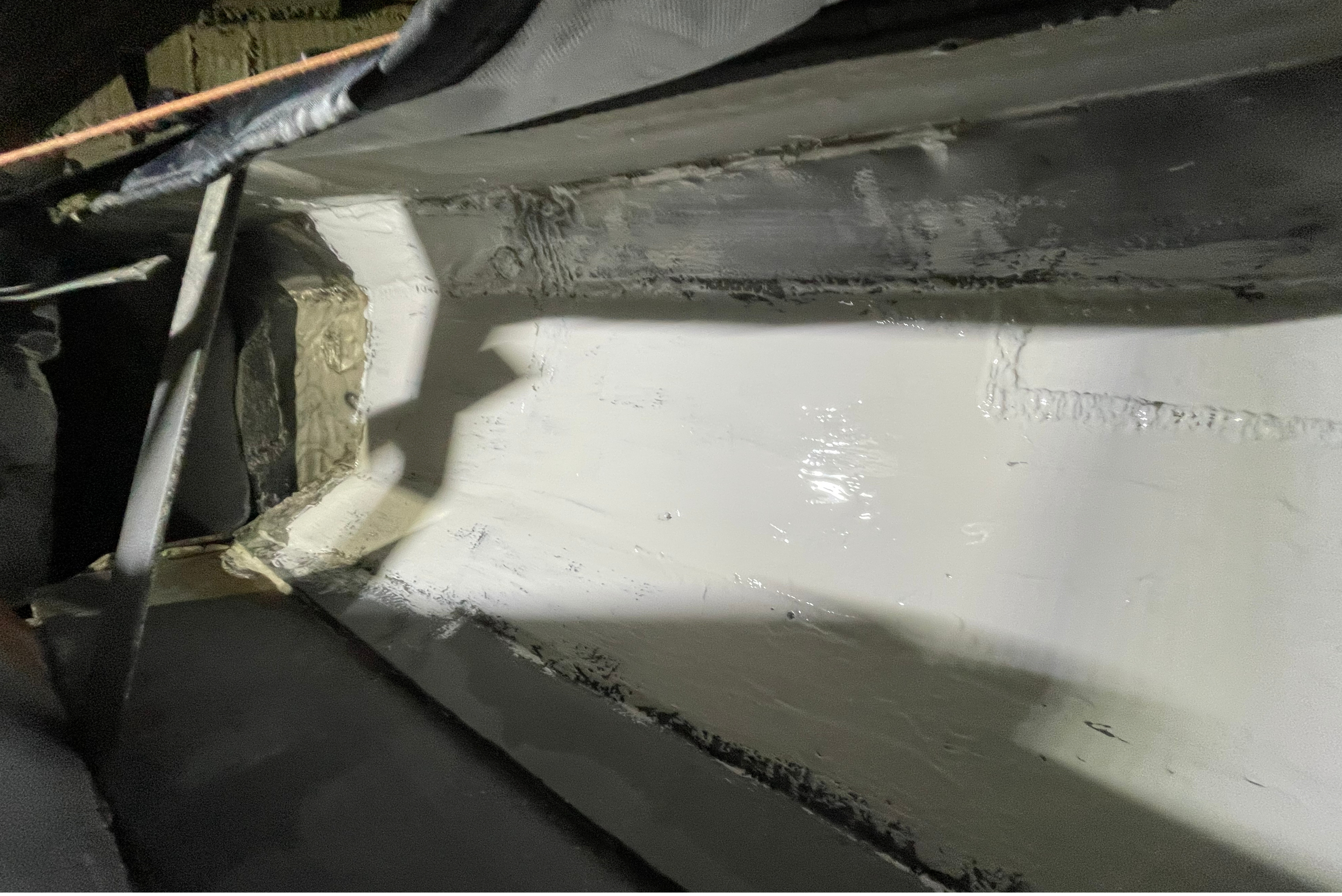 Vue intérieure d'une goulotte ou d'une trémie métallique partiellement enduite d'une protection blanche brillante.