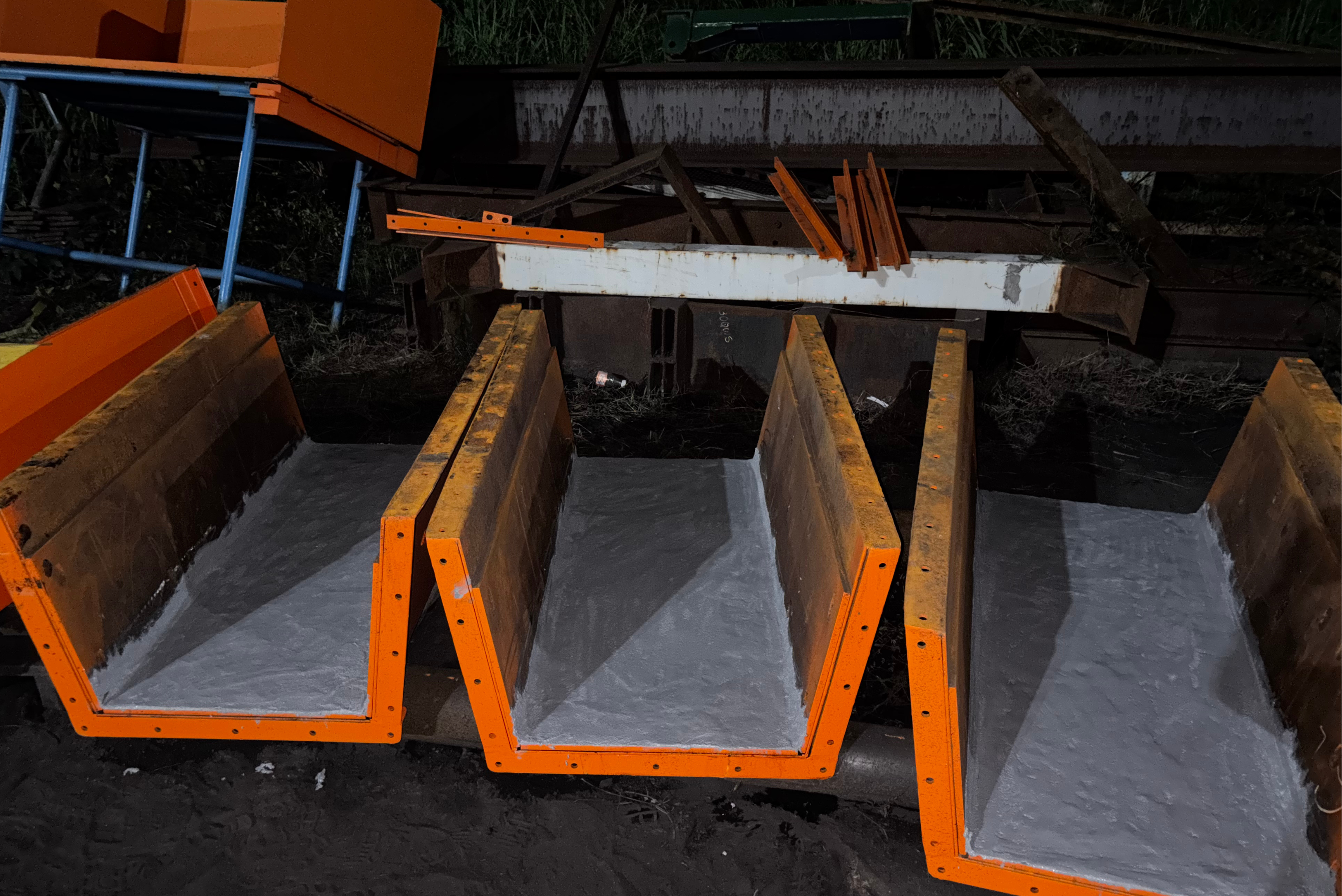 Plusieurs goulottes ou segments de canaux en U aux bords extérieurs orange vif et dotés d'un revêtement de protection intérieur lisse et gris clair, alignés les uns à côté des autres dans un environnement industriel.