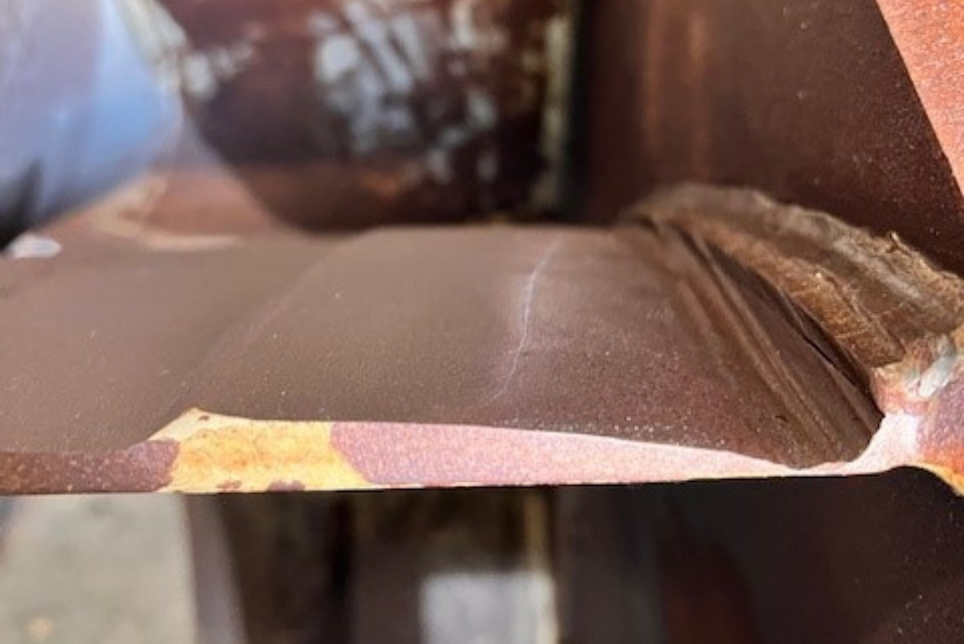 Gros plan sur une pièce métallique industrielle brune présentant une fissure visible le long de sa surface.