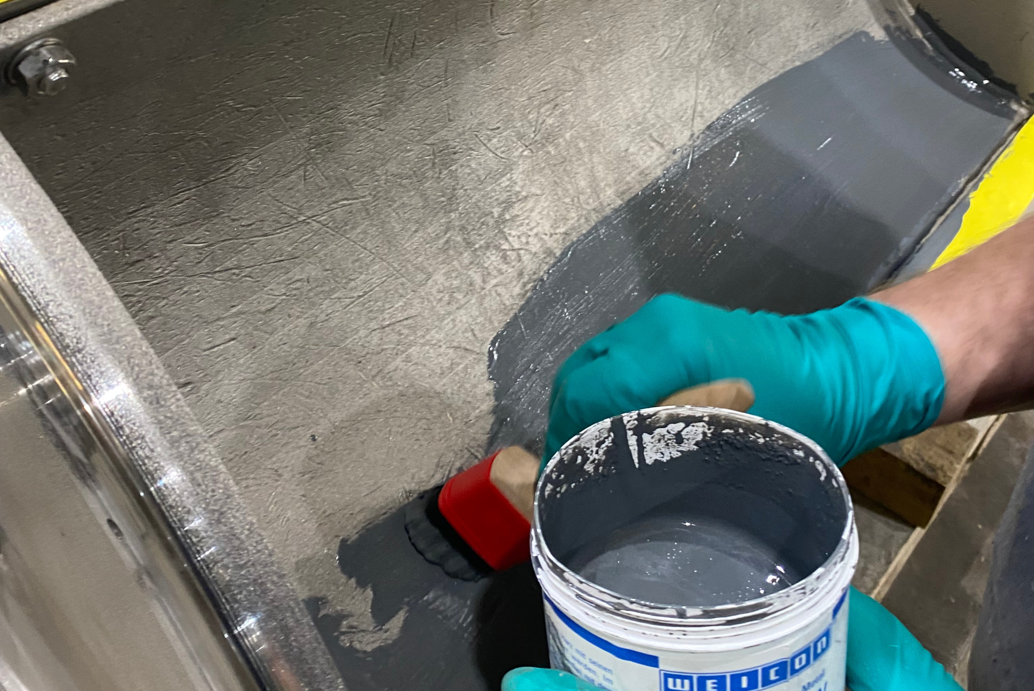 Gros plan sur une personne portant des gants de protection verts et appliquant une couche de revêtement gris foncé ou de peinture protectrice sur la surface intérieure