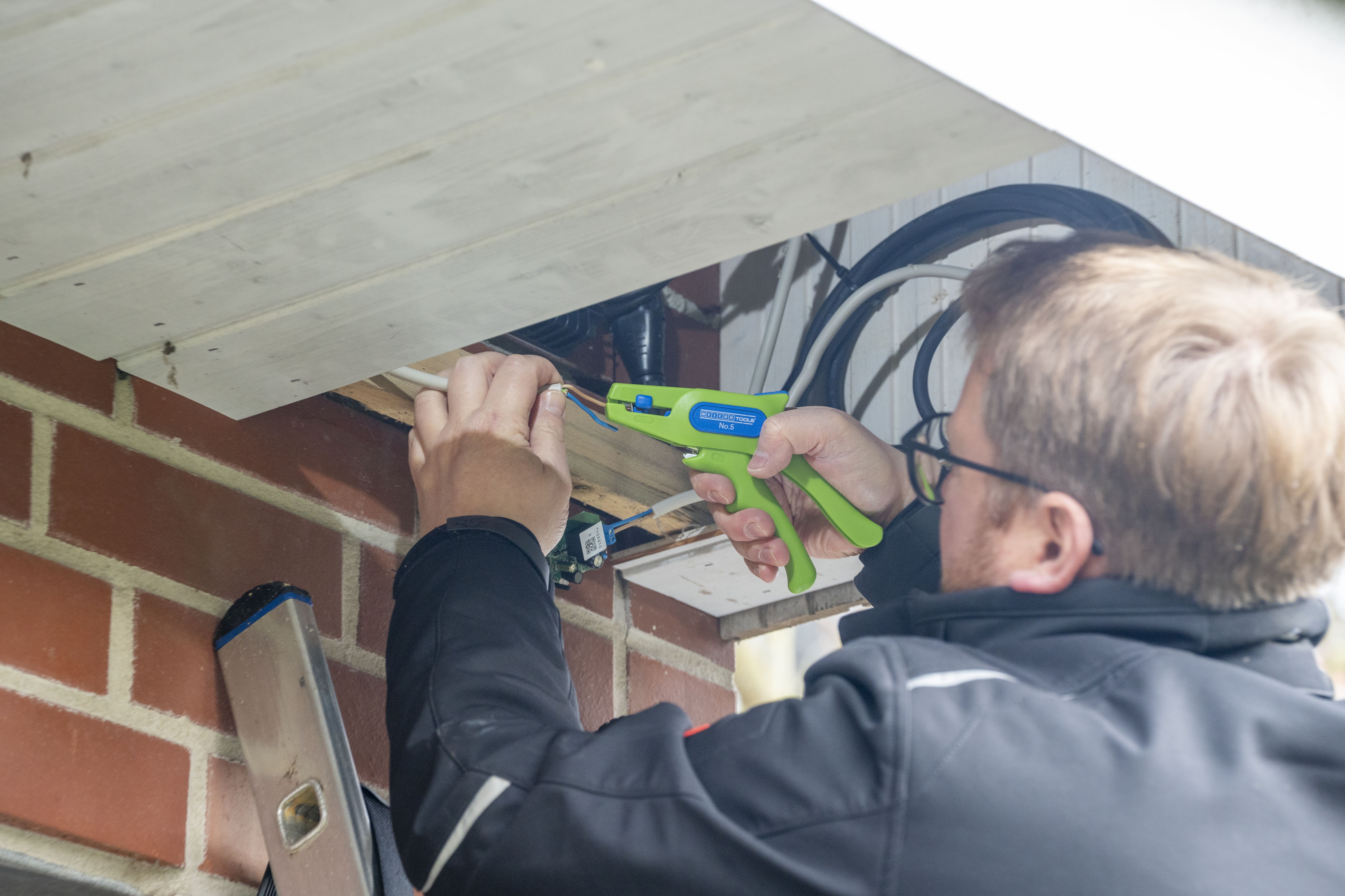 Ein Mann isoliert an einer Hauswand ein Kabel  mit der Green Line Abisolierzange No. 5 ab
