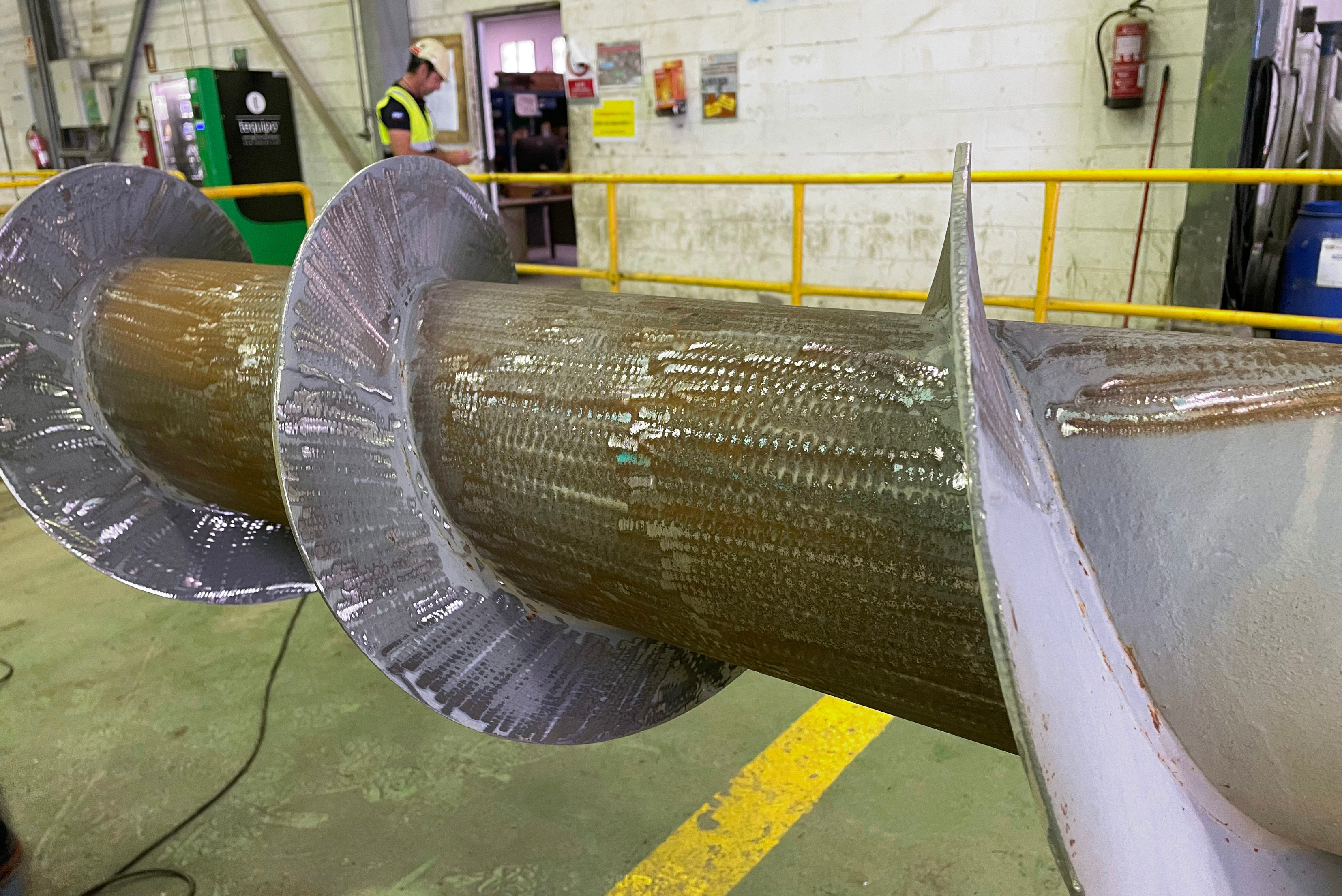 Gros plan sur une grande vis sans fin industrielle dotée de pales hélicoïdales enduites d'un revêtement protecteur brillant, dans un atelier