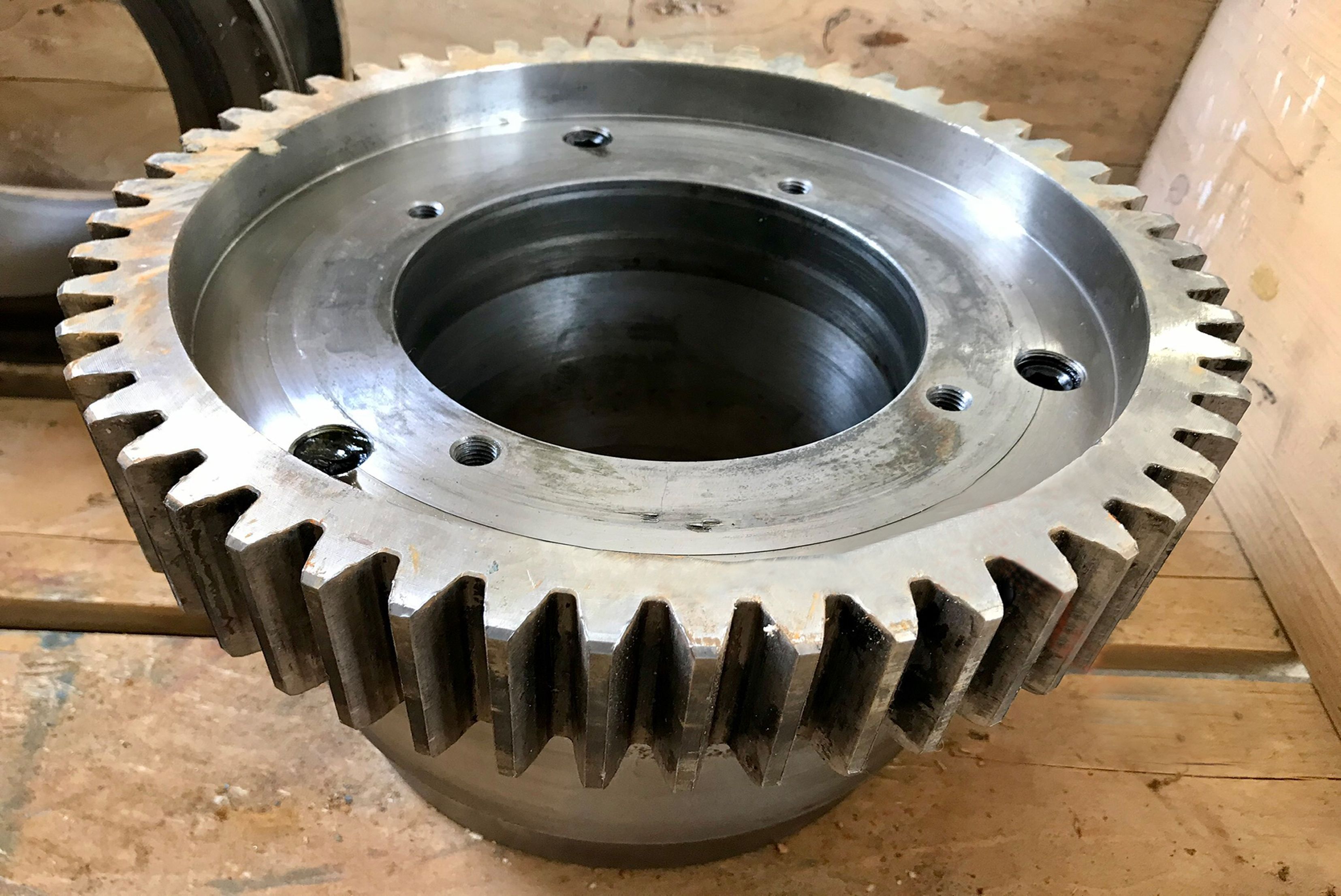 Vue de face d'un grand engrenage industriel métallique usiné avec précision, doté d'une denture extérieure et d'un alésage central, posé sur une surface en bois.