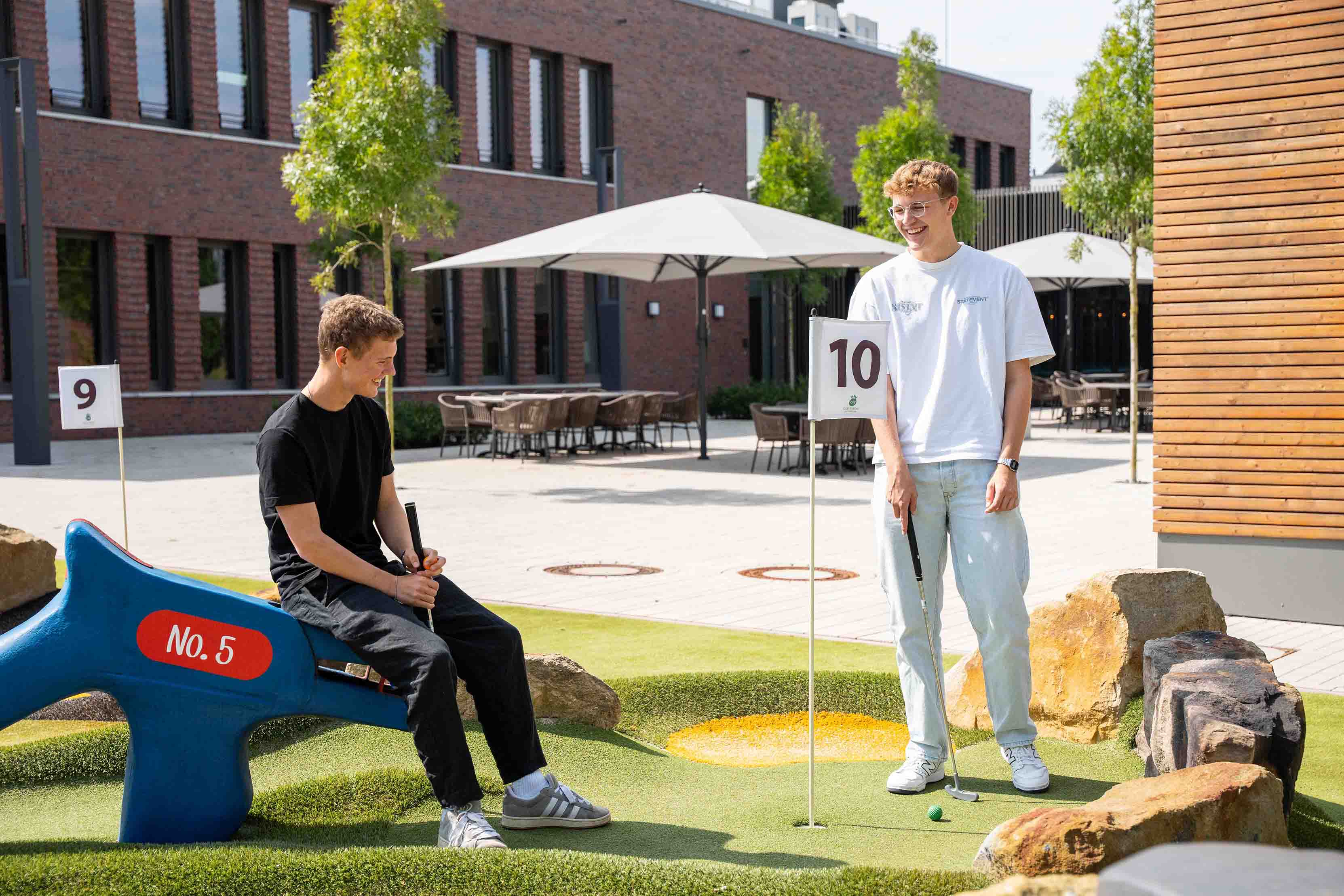 Deux jeunes hommes jouent au minigolf ensemble et rient.